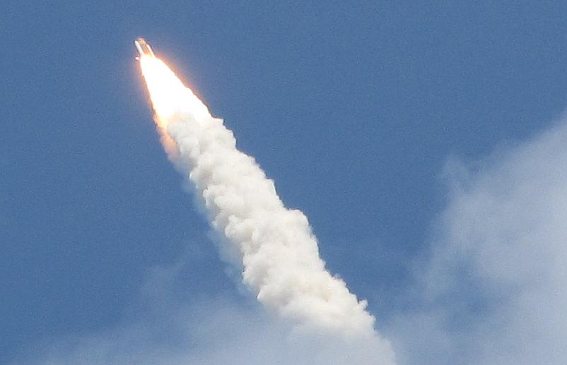 Space Shuttle Atlantis atop a tower of flame and smoke